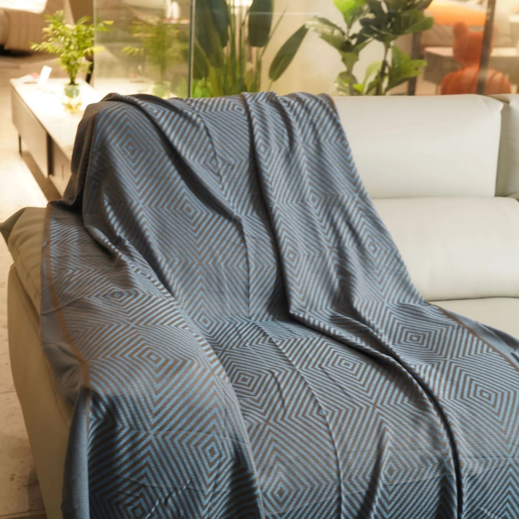 Une couverture décorative noire et grise avec un motif géométrique sur un canapé blanc, dans une pièce avec des plantes vertes.