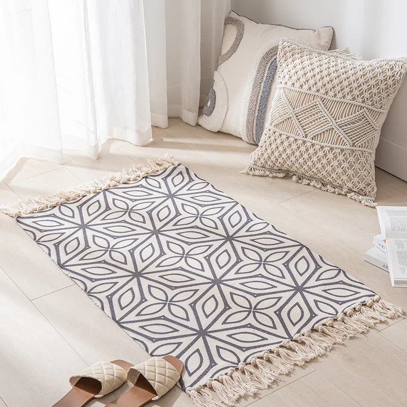 Intérieur douillet avec un tapis gris orné de motifs géométriques et des coussins blancs et beiges texturés, créant une atmosphère apaisante et harmonieuse.