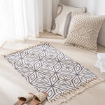 Intérieur douillet avec un tapis gris orné de motifs géométriques et des coussins blancs et beiges texturés, créant une atmosphère apaisante et harmonieuse.