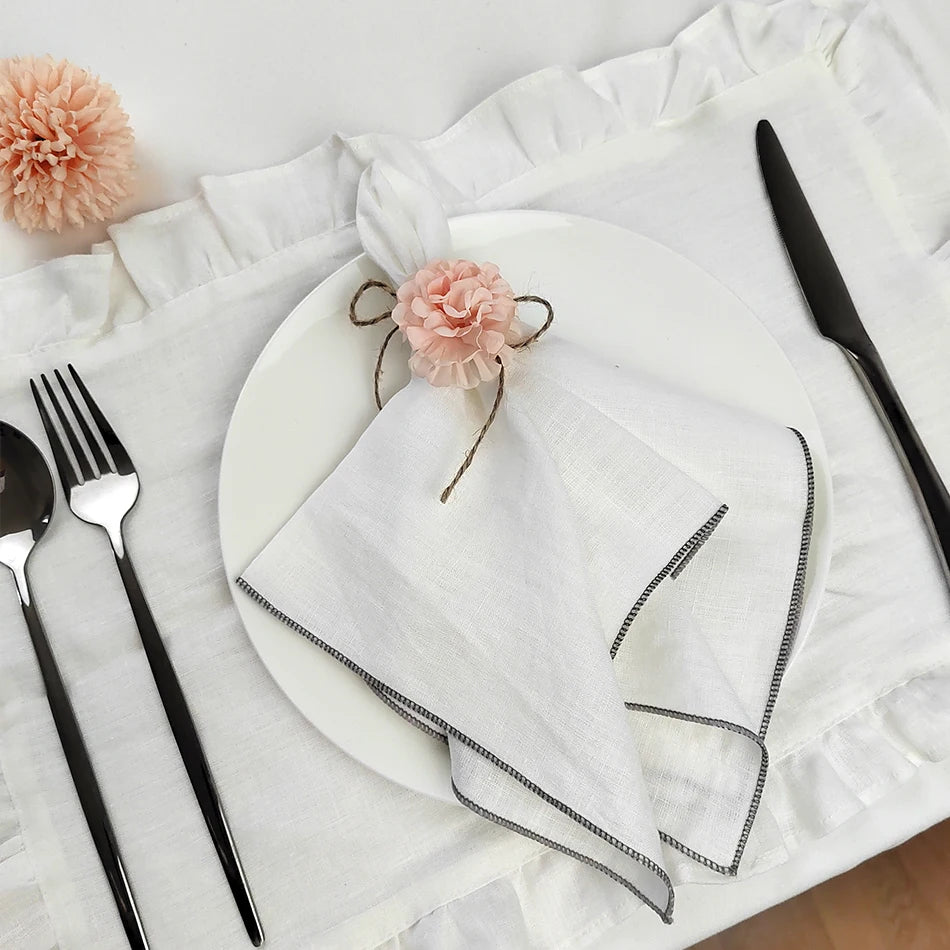 Une table élégante avec des serviettes blanches, des fleurs roses, des couverts et une décoration délicate.