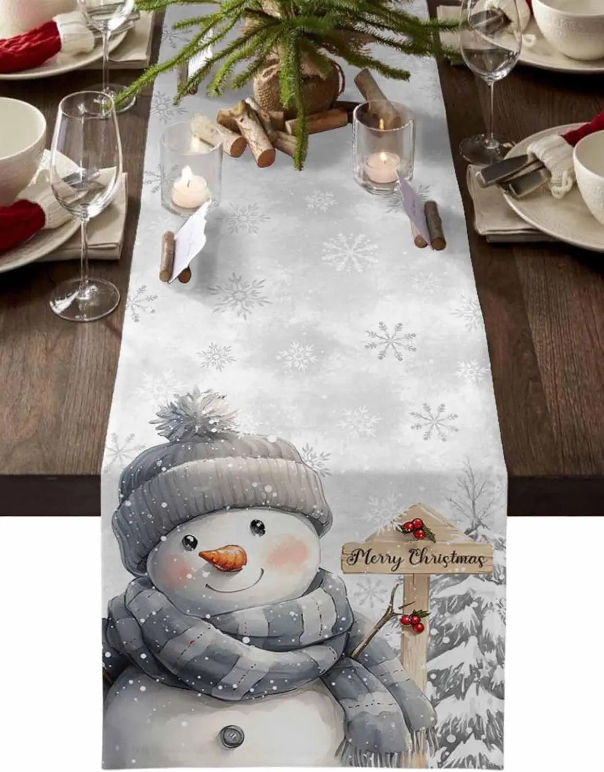 Une table de Noël élégante avec une nappe à motifs de flocons de neige et un adorable bonhomme de neige en peluche, créant une ambiance festive et chaleureuse.