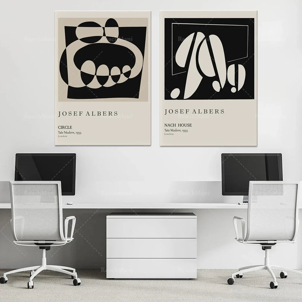 Deux affiches d'art abstrait avec des formes géométriques noires et blanches, encadrées au mur, entourant un bureau moderne avec deux chaises de bureau blanches.