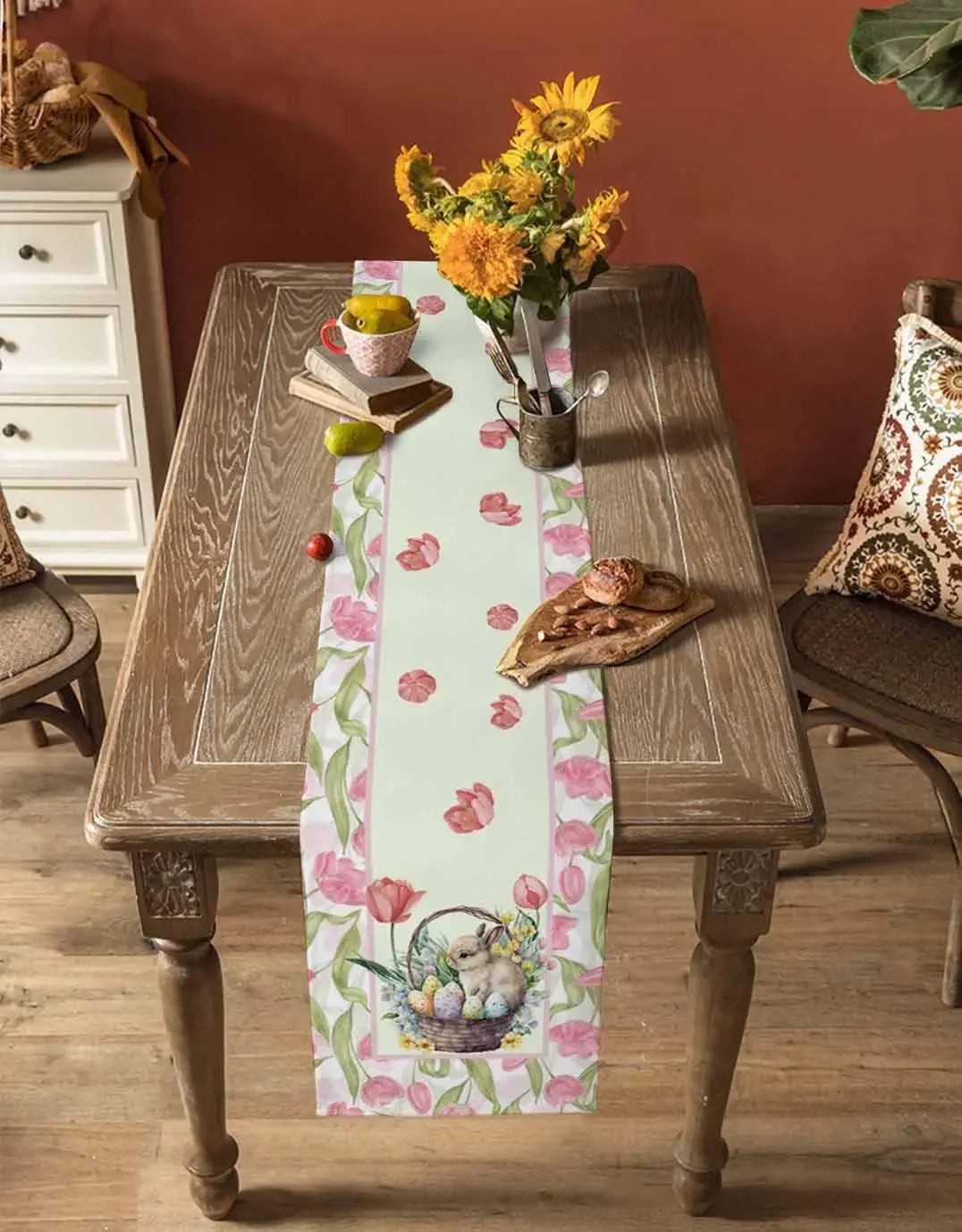 Une table en bois rustique décorée avec un bouquet de tournesols, une coupe de fruits et un livre, le tout sur un chemin de table fleuri.