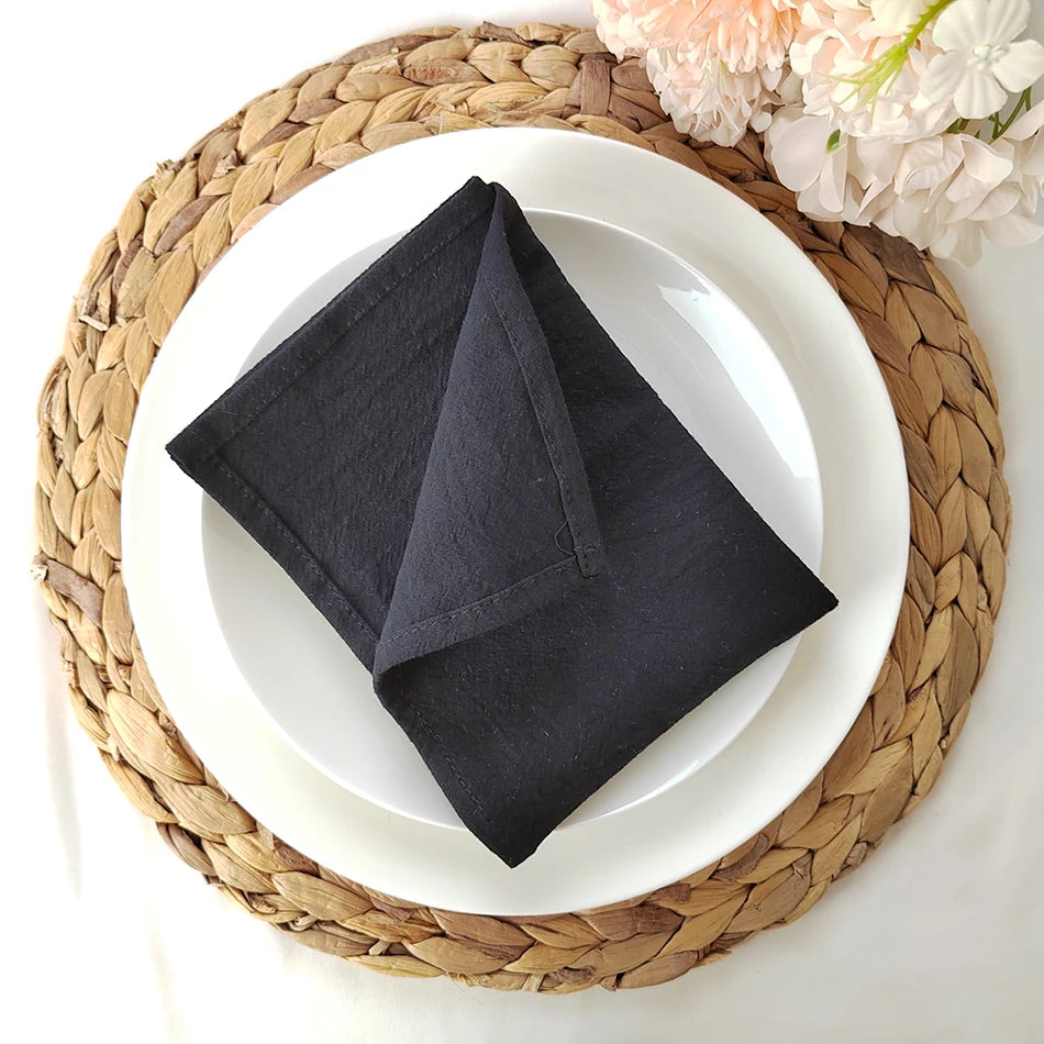 Un plat blanc avec une serviette de table noire pliée et des fleurs roses, posé sur un tapis en fibre tressée.