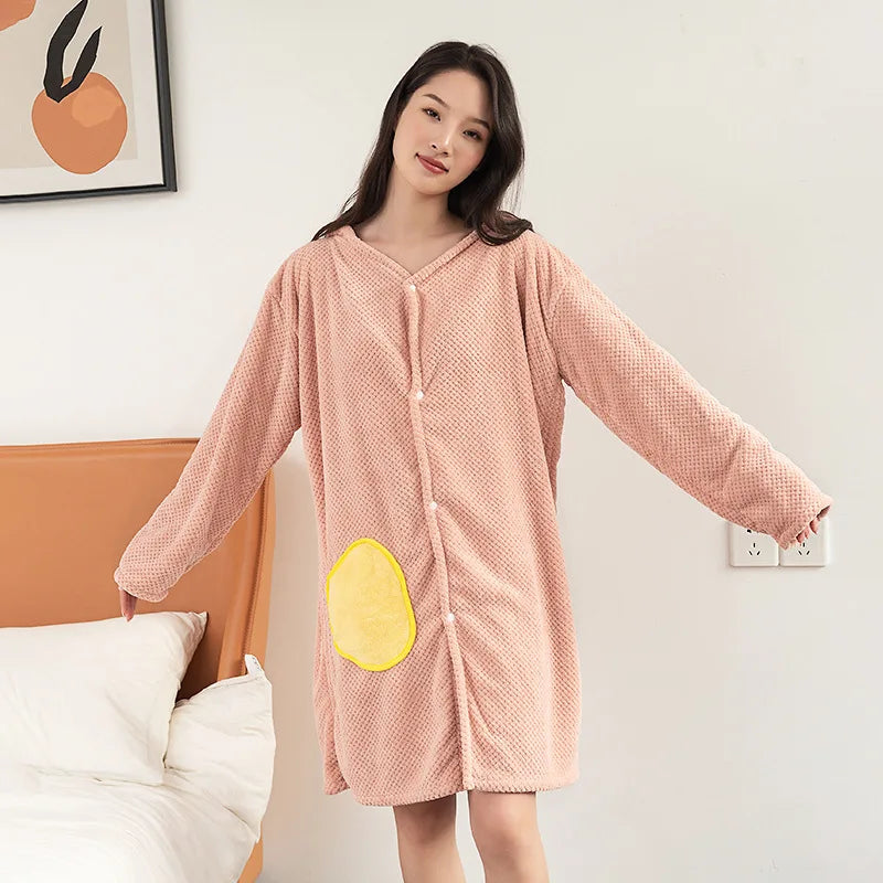 Le modèle porte une robe rose de style cocooning avec un motif textural et une grande poche jaune sur le devant, créant une tenue confortable et originale dans un environnement domestique accueillant.