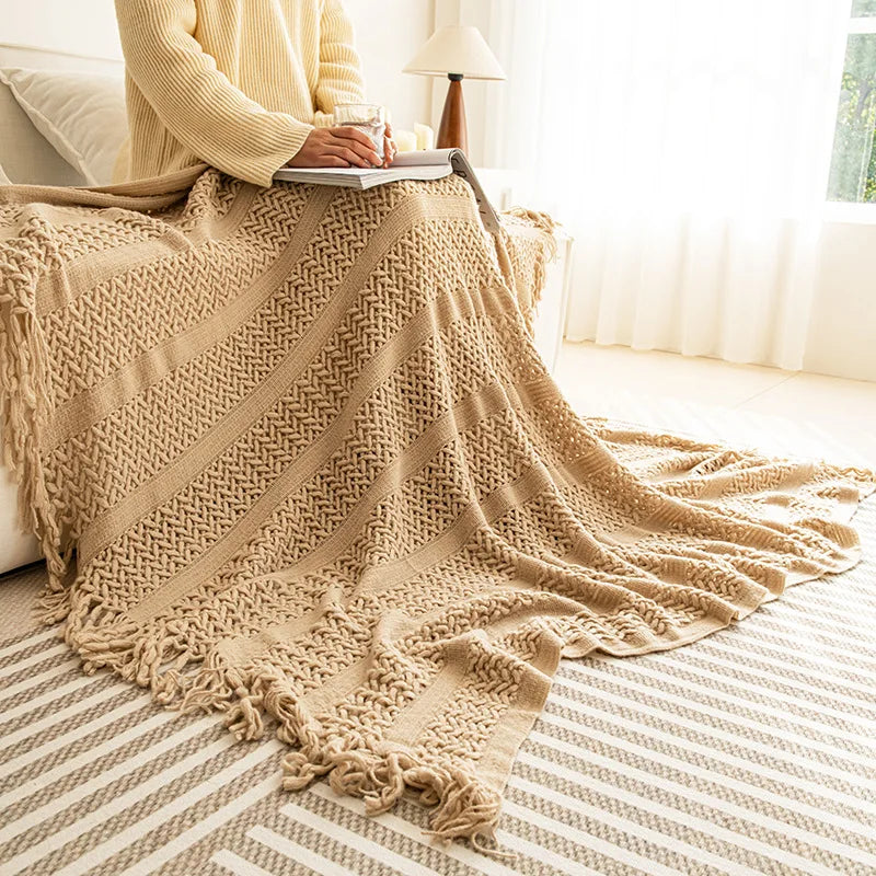 Une couverture beige en tricot aux motifs texturés, disposée sur un canapé dans une pièce lumineuse et accueillante.