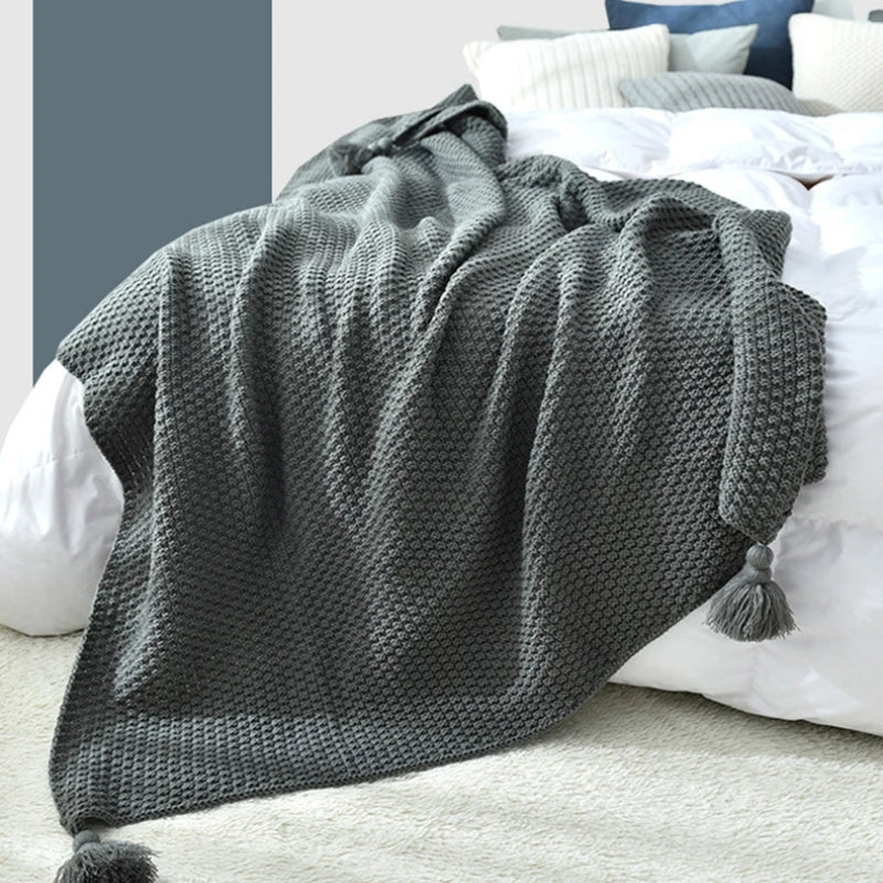 Couverture en tricot grise douillette sur un lit blanc et bleu.