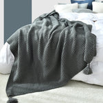 Couverture en tricot grise douillette sur un lit blanc et bleu.