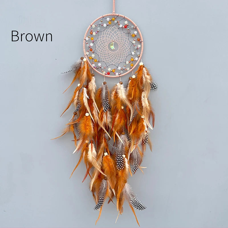 Un capteur de rêves artisanal avec des plumes de couleur marron, orange et blanc, ainsi que des perles et des pierres.