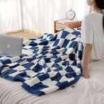 Une couverture douce et confortable aux motifs géométriques bleus et blancs recouvre un espace de travail cocooning, prêt à accueillir un ordinateur portable sur un lit aux couleurs apaisantes.