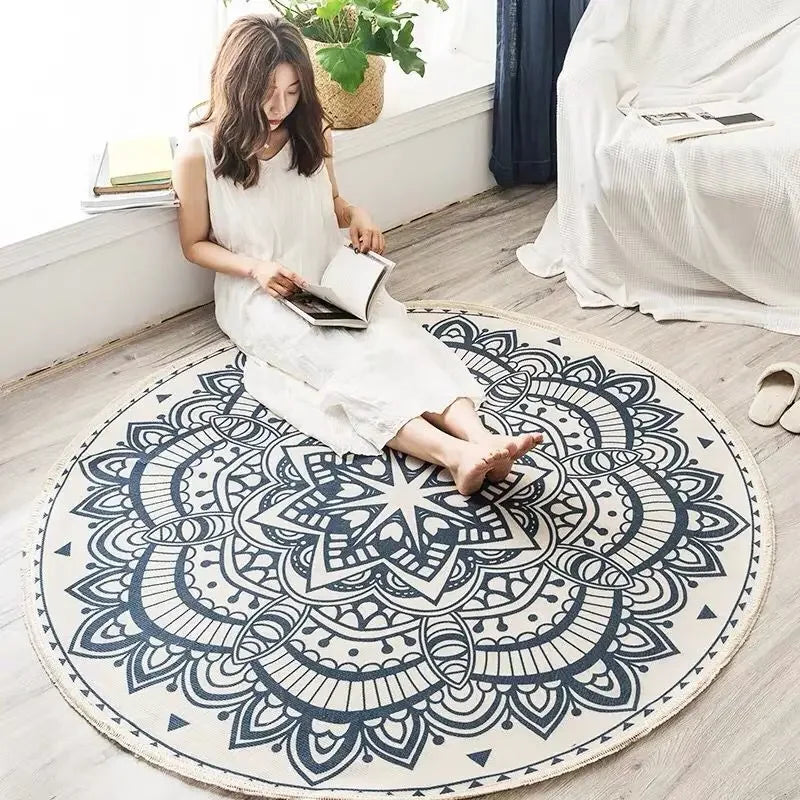 Une femme assise sur un tapis rond orné de motifs décoratifs noirs et blancs, lisant attentivement un livre.