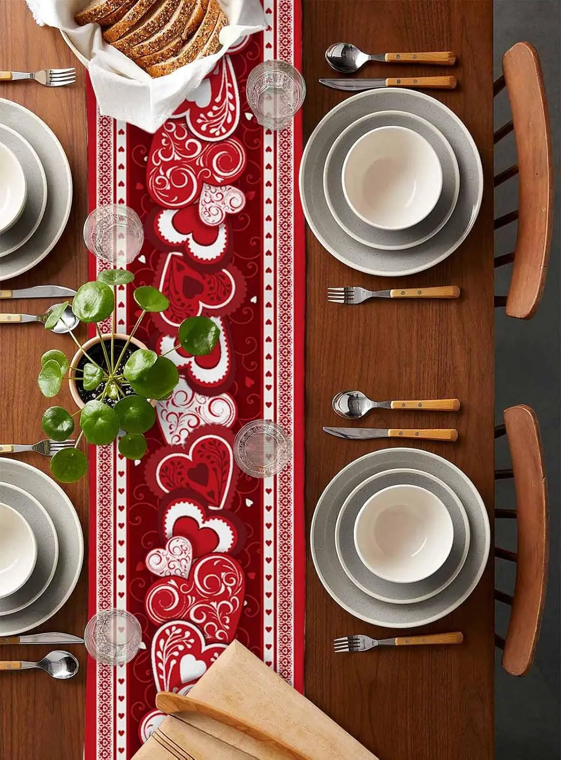 Une table joliment dressée avec des assiettes blanches, des couverts en bois et un chemin de table rouge orné de motifs de coeurs.