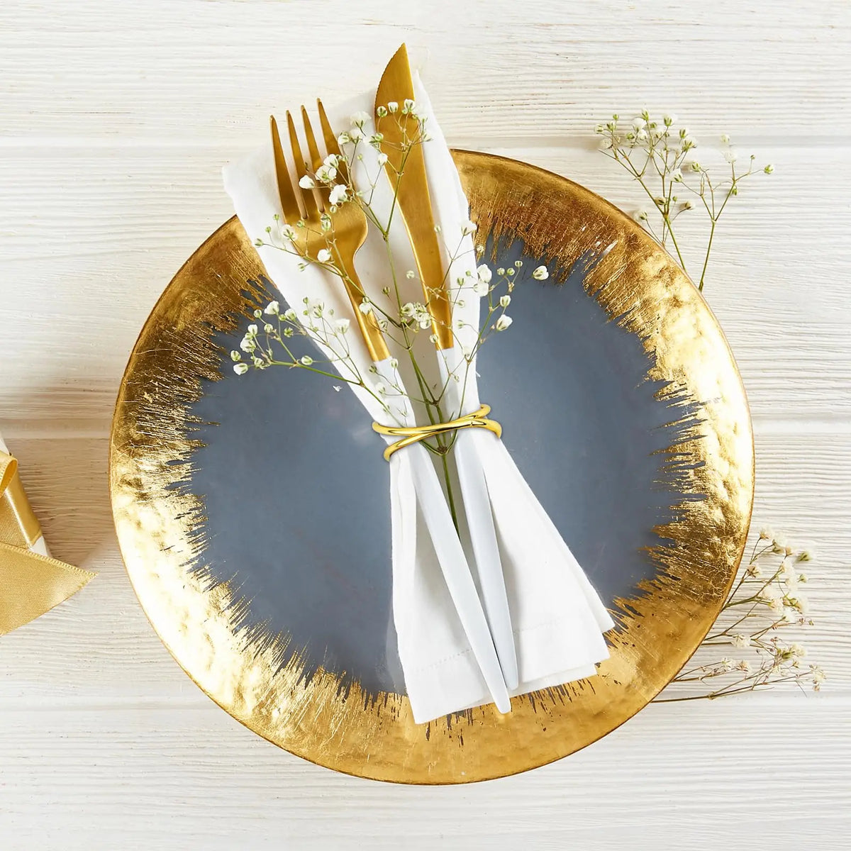 Assiette dorée élégante avec couverts et décoration florale, créant une table dressée de manière sophistiquée.