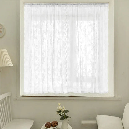 Voilage blanc court à motifs floraux, habillant une petite fenêtre dans un intérieur lumineux.