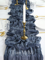 Une table dressée avec une nappe bleue sombre, des verres cristallins, des couverts en métal doré et une bougie blanche sur un chandelier doré.