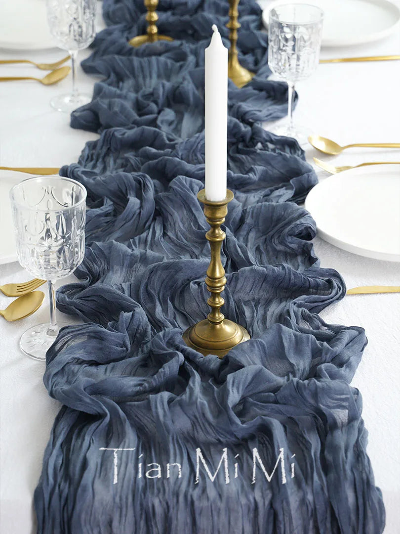 Une table dressée avec une nappe bleue sombre, des verres cristallins, des couverts en métal doré et une bougie blanche sur un chandelier doré.