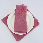 Serviette de table rose ornée d'une branche de fleurs séchées, sur une assiette blanche, sur un fond blanc.