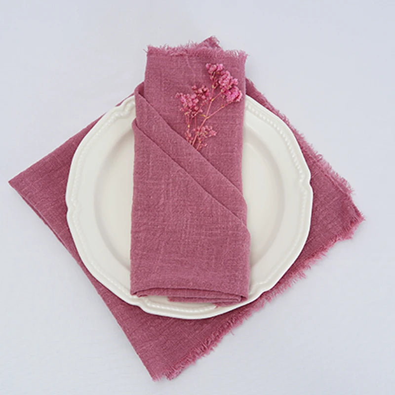 Serviette de table rose ornée d'une branche de fleurs séchées, sur une assiette blanche, sur un fond blanc.