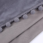 Gros plan sur les finitions pompons gris cousus sur un tissu en velours gris clair, mettant en valeur la texture du rideau.