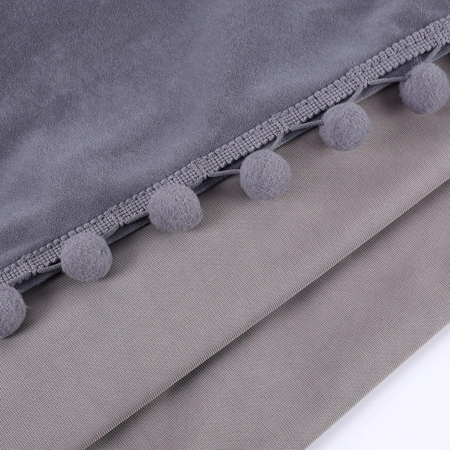 Gros plan sur les finitions pompons gris cousus sur un tissu en velours gris clair, mettant en valeur la texture du rideau.