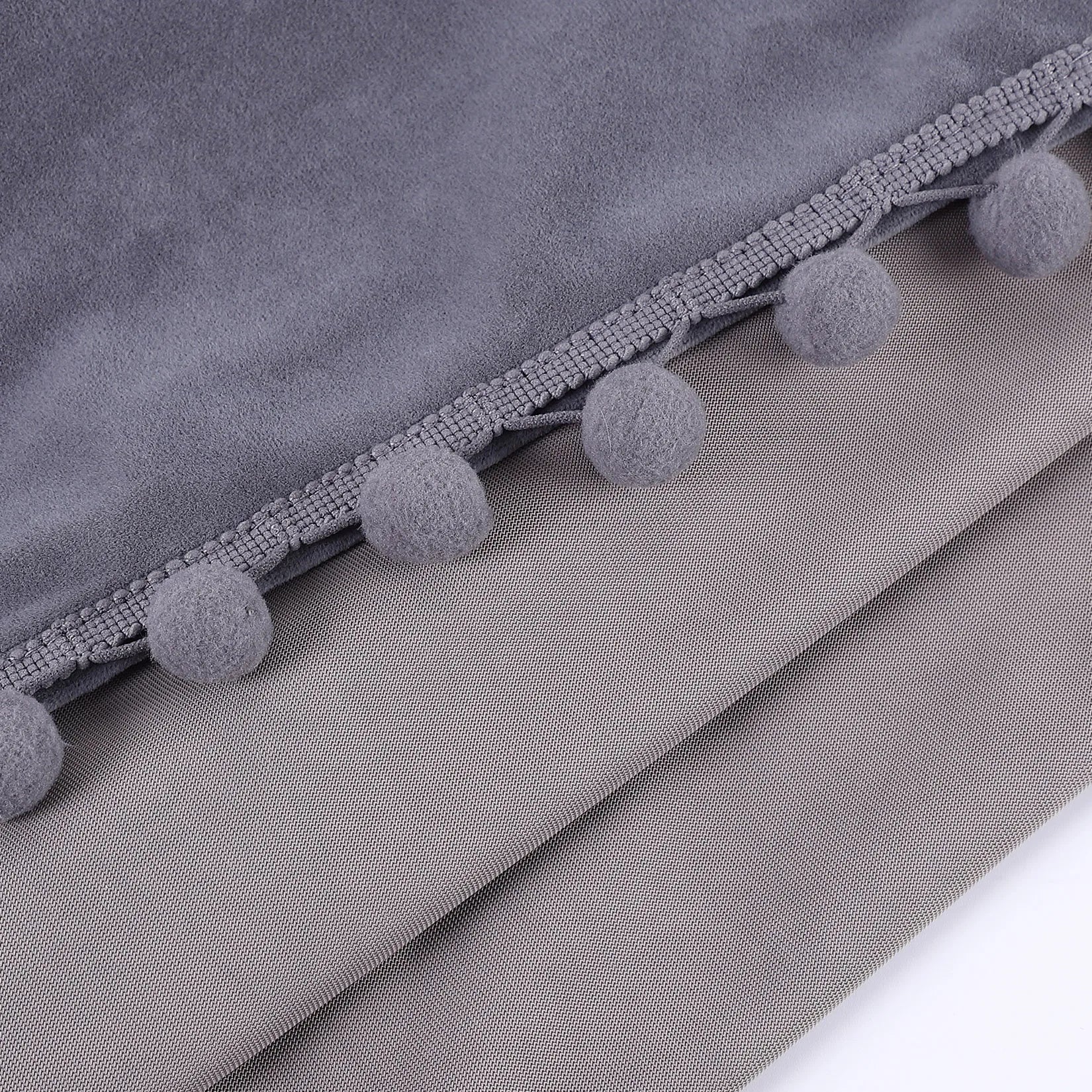 Gros plan sur les finitions pompons gris cousus sur un tissu en velours gris clair, mettant en valeur la texture du rideau.