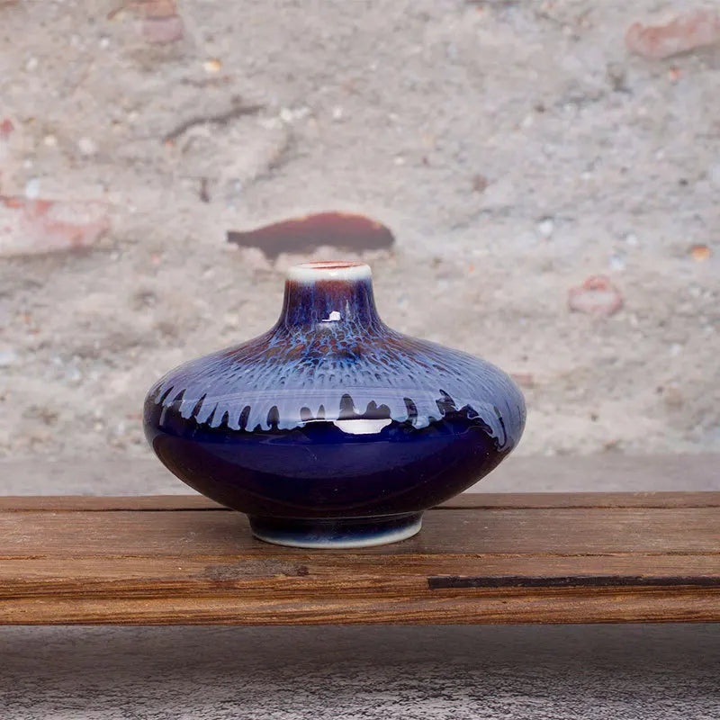 Un vase en céramique de style japonais avec des motifs bleus et rouges sur un fond gris foncé, posé sur une surface en bois.