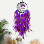 L'image montre un attrapeur de rêves décoratif avec des plumes violettes et roses qui pendent de l'anneau noir en forme de lune, créant une belle et mystique pièce de décoration.