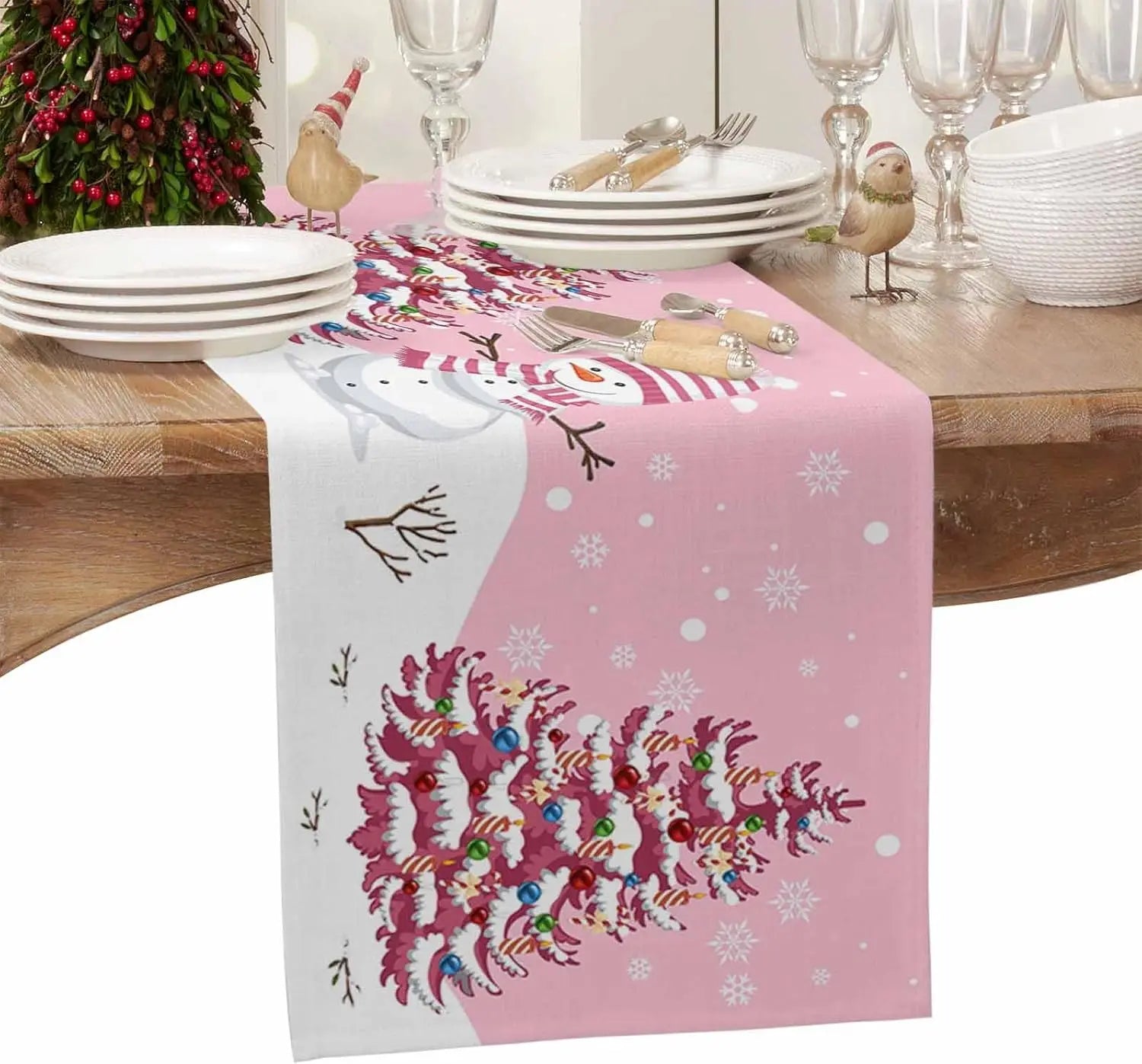 Une table festive avec des assiettes, des verres et une nappe rose décorée de motifs hivernaux et d'un tapis de table en forme de bonhomme de neige.