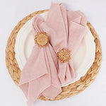 Assiette en osier avec serviette rose pastel et décorations florales dorées.