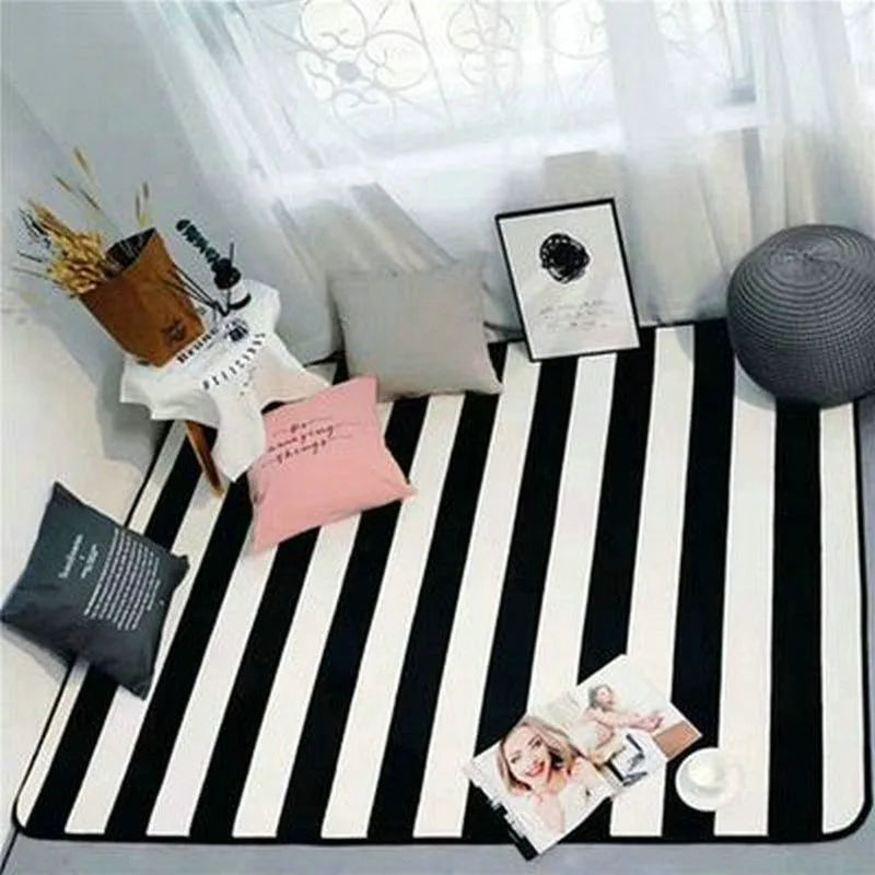 Cette image montre une surface noire et blanche aux motifs rayés, sur laquelle sont disposés divers objets décoratifs, notamment des cadres photos, des boules de laine et des stylos.