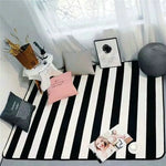 Cette image montre une surface noire et blanche aux motifs rayés, sur laquelle sont disposés divers objets décoratifs, notamment des cadres photos, des boules de laine et des stylos.