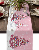 La table festive présente une nappe rose ornée d'un design de sapin de Noël avec des branches décorées de boules colorées, ainsi que d'un personnage de bonhomme de neige souriant au centre.