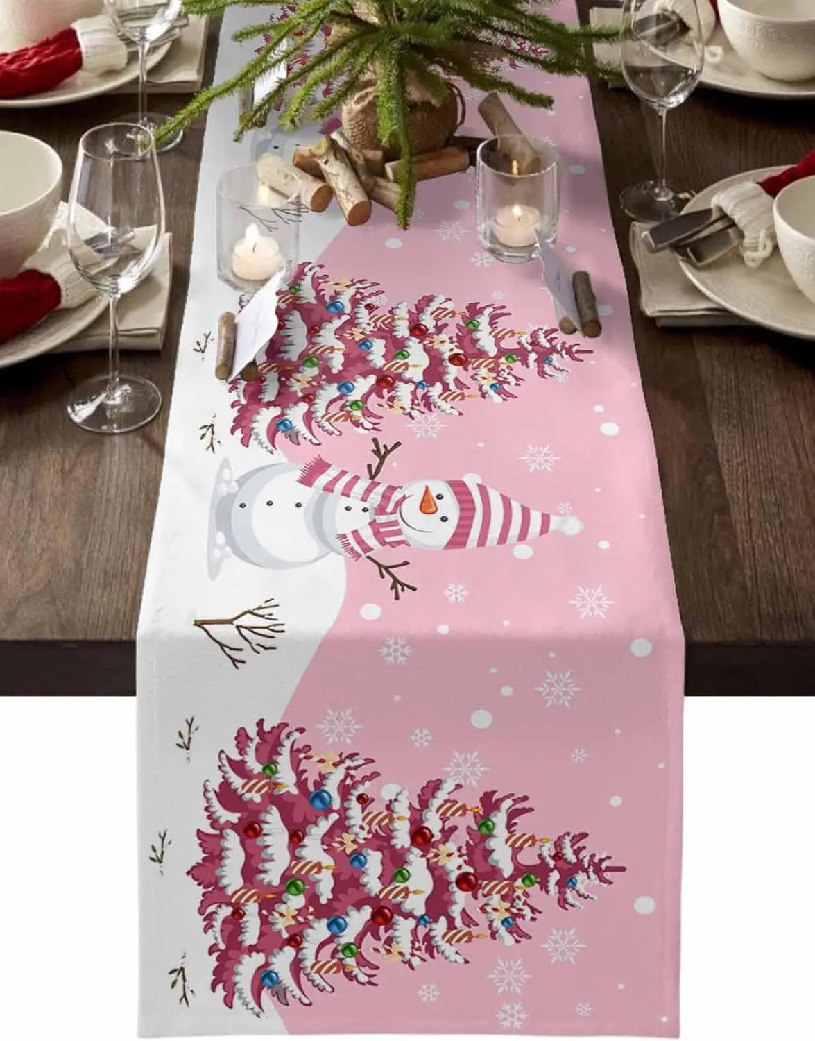 La table festive présente une nappe rose ornée d'un design de sapin de Noël avec des branches décorées de boules colorées, ainsi que d'un personnage de bonhomme de neige souriant au centre.