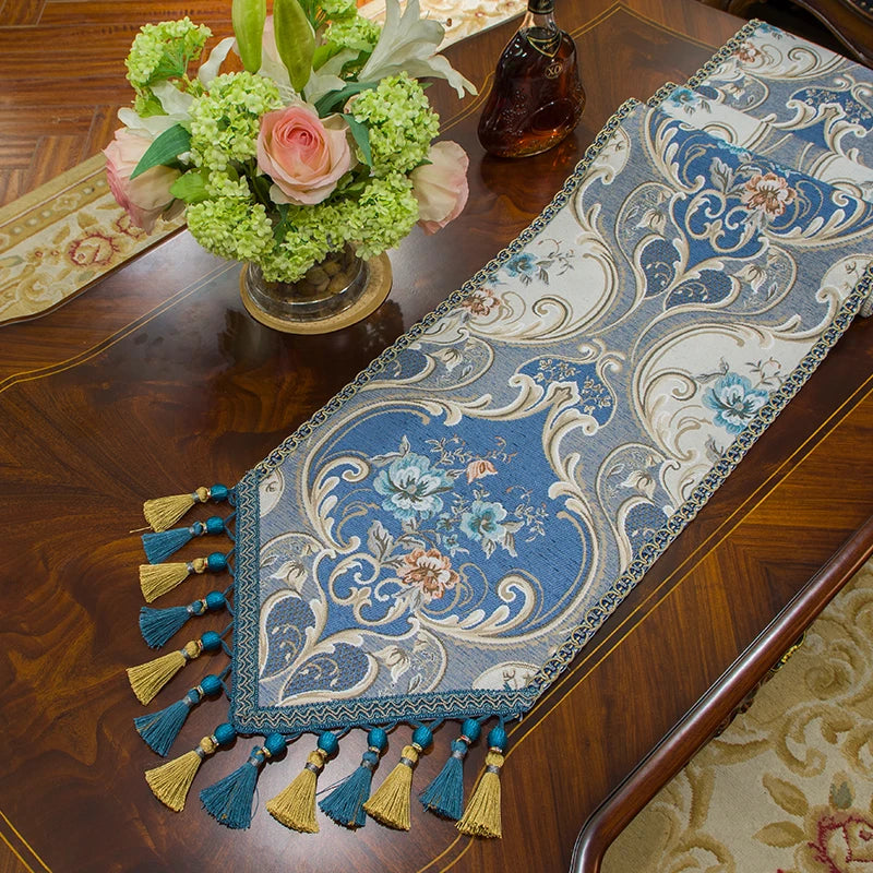 Une élégante tenture de table bleu et or ornée de fleurs aux couleurs chatoyantes, disposée sur un meuble en bois sombre avec un bouquet floral raffiné, créant une atmosphère chaleureuse et harmonieuse.