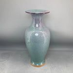 Un vase en verre coloré avec un design texturé et une forme élégante, posé sur une surface brillante.