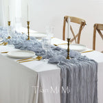 Une table élégante dressée pour un repas spécial, avec des assiettes blanches, des verres en cristal, des bougeoirs dorés et une nappe grise plissée.