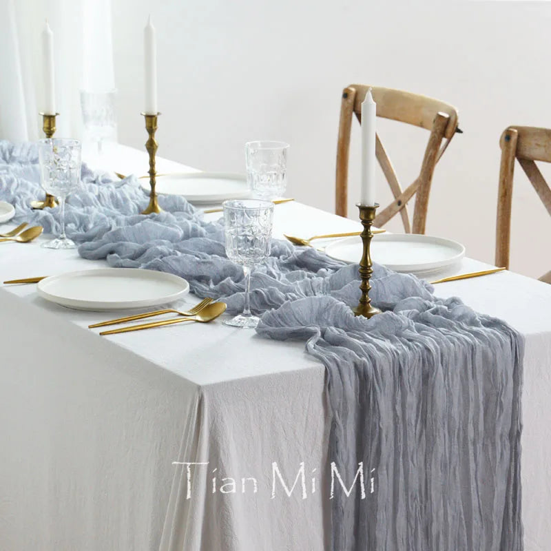 Une table élégante dressée pour un repas spécial, avec des assiettes blanches, des verres en cristal, des bougeoirs dorés et une nappe grise plissée.
