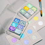 peintures aquarelle palette compacte bleu vert violet rose beige jaune blanc texture granuleuse opaques