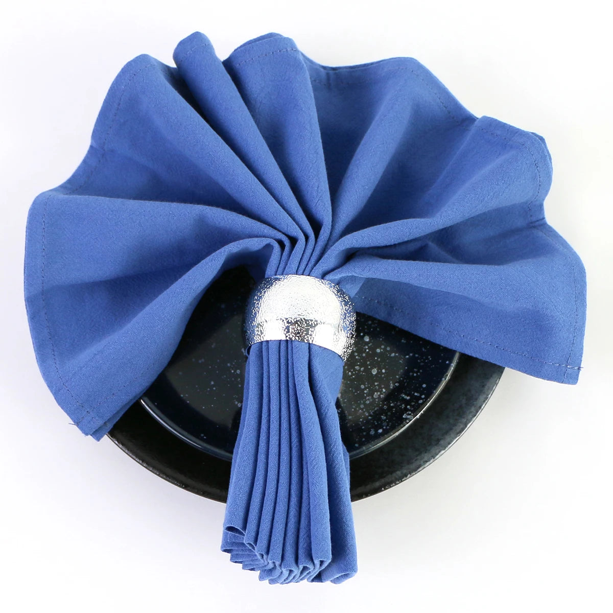 Cette élégante serviette bleue enroulée autour d'un plat noir et argenté crée une décoration de table raffinée et invitante.
