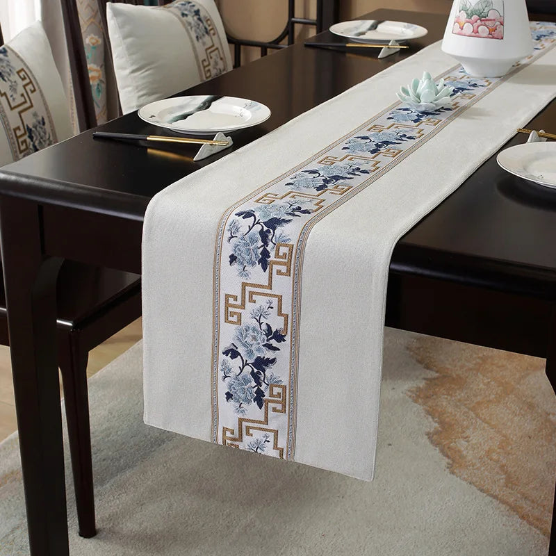 La nappe de table élégante présente une bordure ornée de fleurs bleues et de motifs géométriques dorés, ajoutant une touche raffinée et sophistiquée à ce cadre de salle à manger.