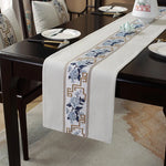 La nappe de table élégante présente une bordure ornée de fleurs bleues et de motifs géométriques dorés, ajoutant une touche raffinée et sophistiquée à ce cadre de salle à manger.