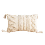 Coussin décoratif en coton beige avec des motifs texturés et des franges, offrant un style bohème et douillet.