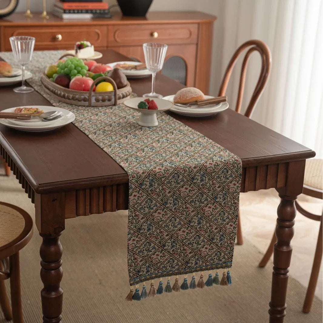 Une table dressée dans un intérieur cosy, avec des plats et des boissons, sur un chemin de table aux motifs floraux et des pompons colorés.