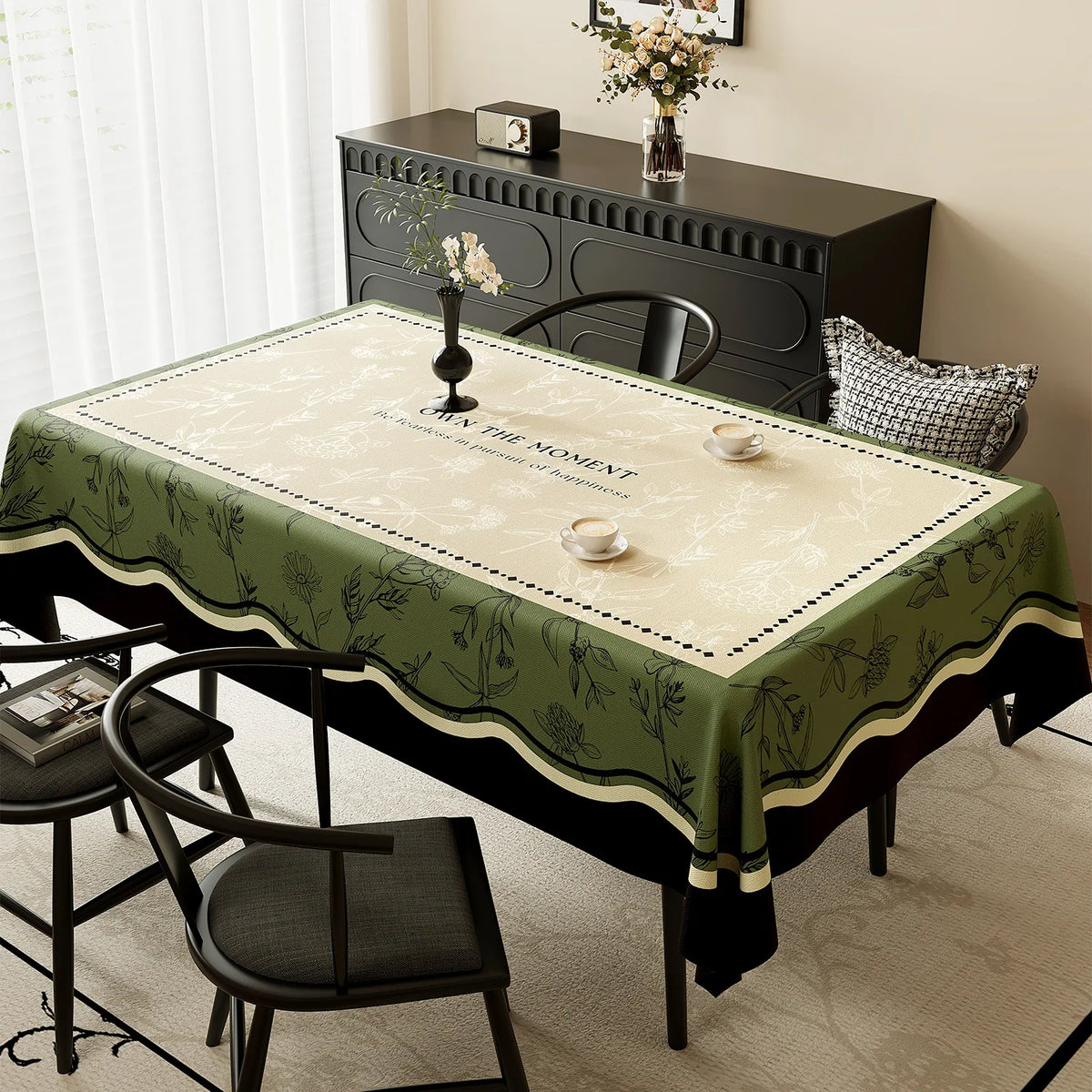 Une table élégante avec un décor floral sur une nappe verte, avec un meuble en bois sombre et un vase de fleurs blanches sur la surface.