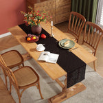 Une belle table en bois avec une nappe noire à motifs, des fleurs colorées, des fruits et des assiettes dressées pour un repas confortable dans un intérieur chaleureux.