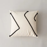 Coussin blanc cassé avec des motifs graphiques noirs en forme de flèches stylisées, créant une image moderne et épurée.