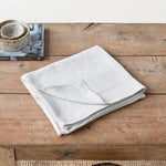 Un détail de nature morte simple avec une pile de serviettes en lin blanc sur une surface en bois texturée.