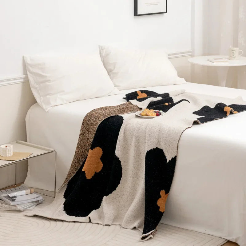 Cette image montre un lit avec une couverture blanche et noire avec des motifs de pâtisseries et de chocolats, créant une ambiance chaleureuse et confortable dans la pièce.