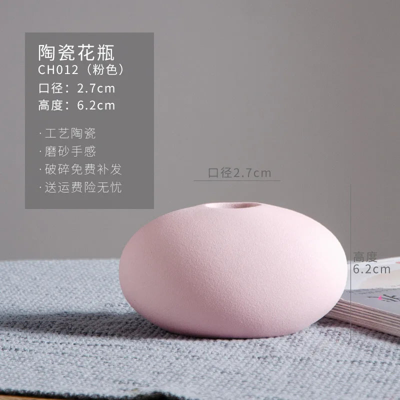 Un vase en céramique de forme ovale, de couleur rose pâle, avec des dimensions de 2,7 cm de diamètre et 6,2 cm de hauteur, offrant une finition mate et une conception élégante.
