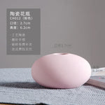 Un vase en céramique de forme ovale, de couleur rose pâle, avec des dimensions de 2,7 cm de diamètre et 6,2 cm de hauteur, offrant une finition mate et une conception élégante.